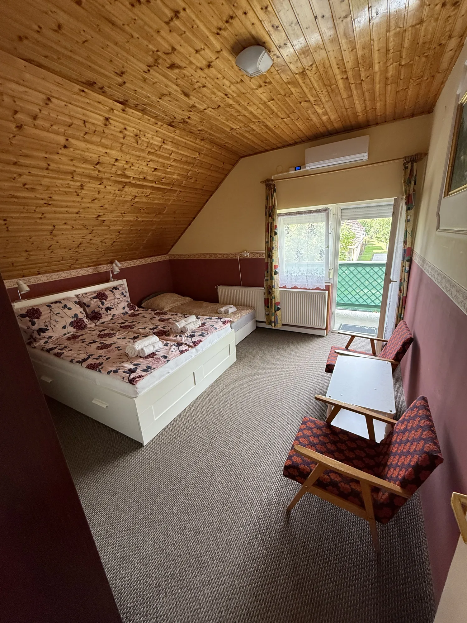 Világos tetőtéri hálószoba a Beáta Apartmanházban kertre néző erkélyajtóval és klímával